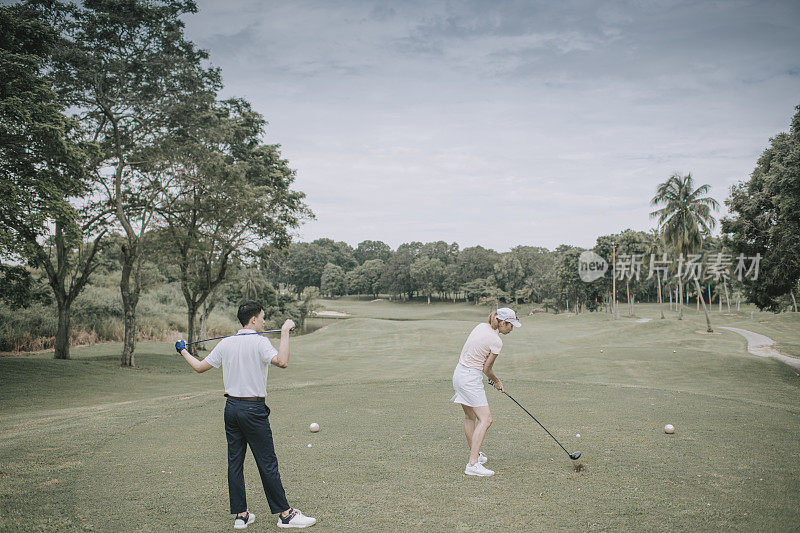 asian chinese female golfer teeing off at golf course with her husband beside